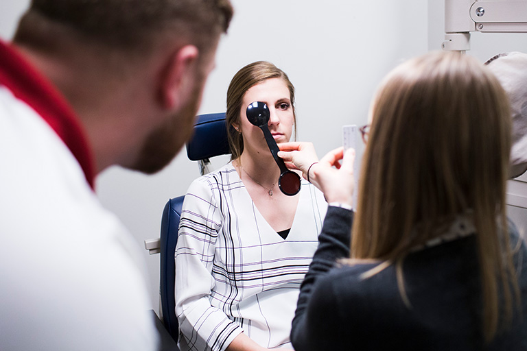 Two optometry students perform an eye exam on a female patient.