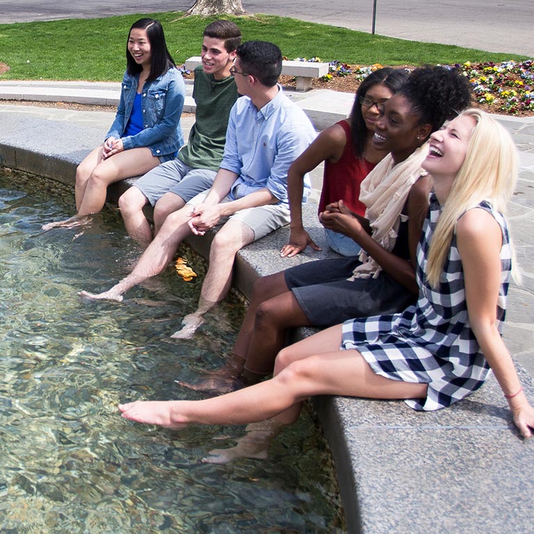 A diverse group of students dip their feet in Showalter Fountain.